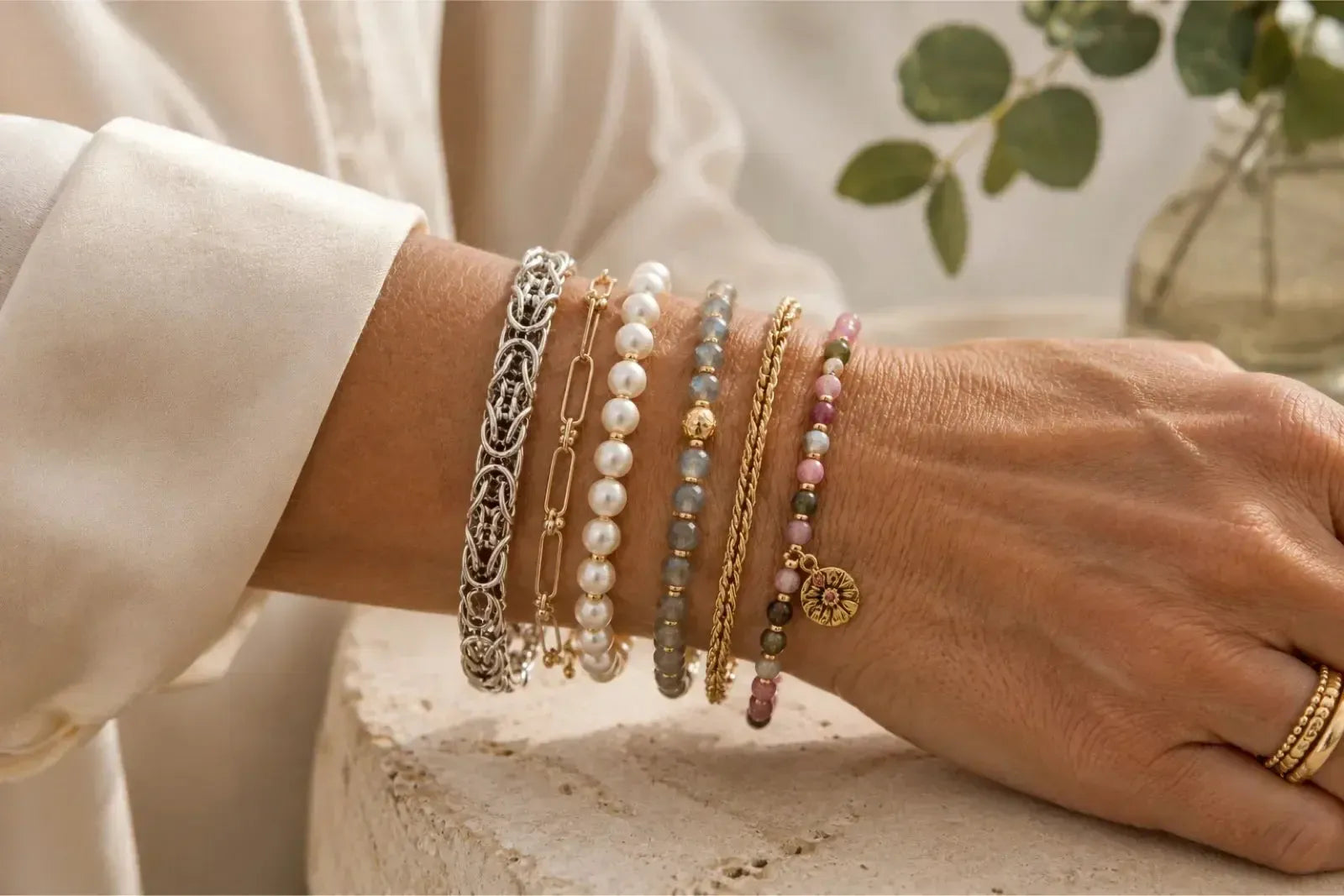 Mature woman wearing a layered bracelet stack with silver, gold, pearls and gemstones for a balanced, personal jewellery look.