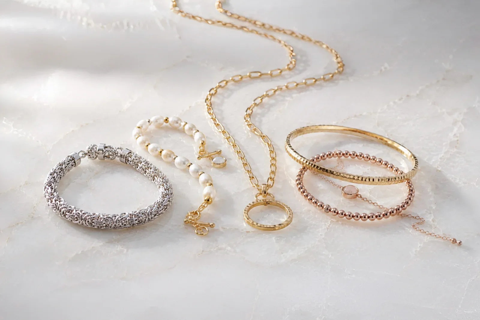 Gold, silver and rose gold jewellery layered with pearls on ivory quartz, illustrating how to mix metals and textures.
