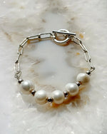 Flat lay of the Callie Freshwater Pearl & Sterling Silver Bracelet featuring luminous freshwater pearls and polished sterling silver links on a soft stone background.