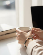 Kaia Pearl Stretch Bracelet styled in a refined lifestyle setting with a coffee cup, highlighting elegant pearl tones and everyday luxury