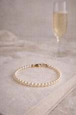 Leilani Cream Pearl Bracelet styled on a soft neutral book with a muted glass of prosecco, capturing timeless elegance and quiet luxury