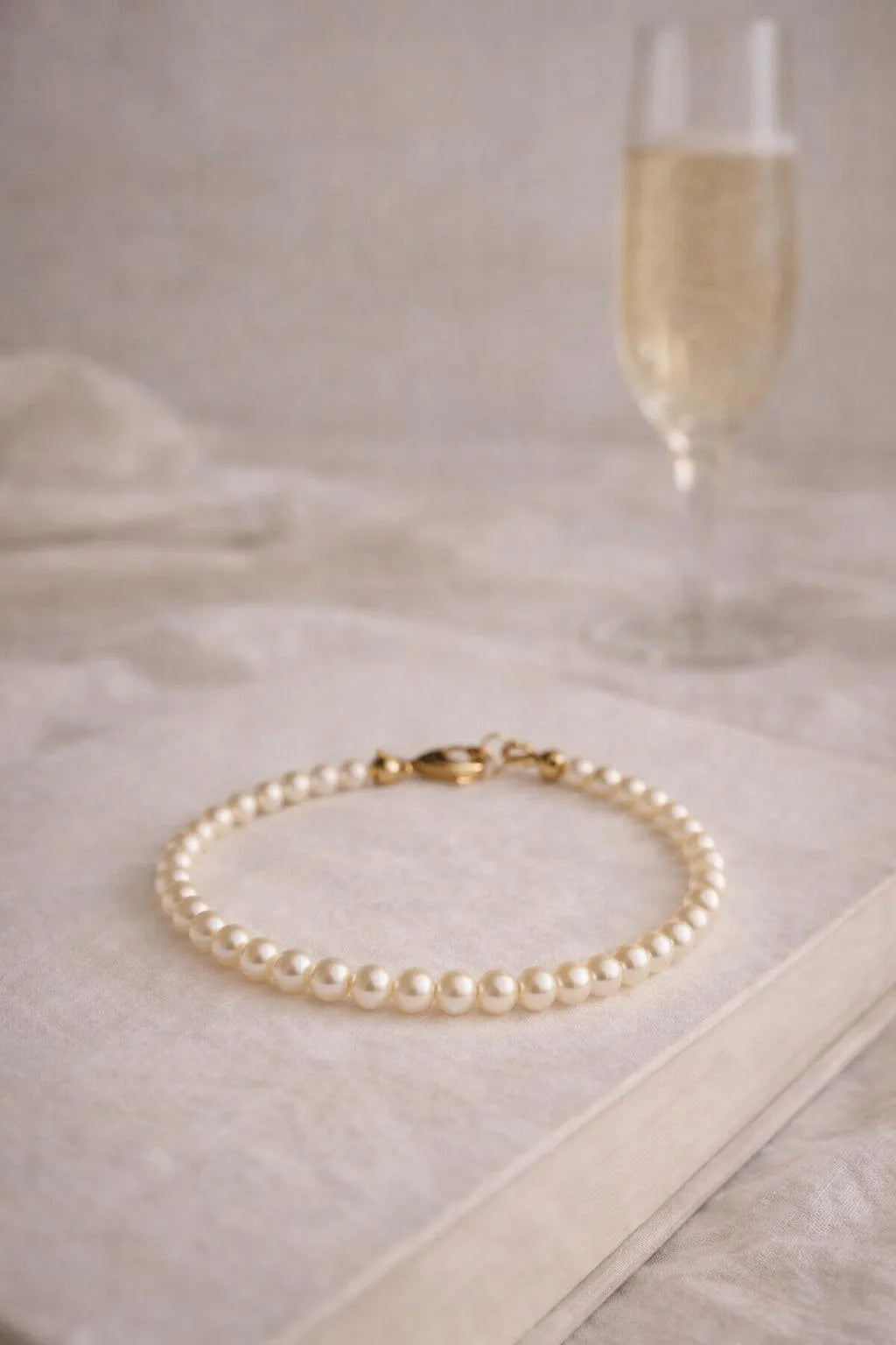 Leilani Cream Pearl Bracelet styled on a soft neutral book with a muted glass of prosecco, capturing timeless elegance and quiet luxury