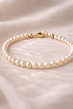 Leilani Cream Pearl Bracelet close-up showing luminous Austrian crystal pearls and a polished 14k gold clasp on a soft neutral fabric background