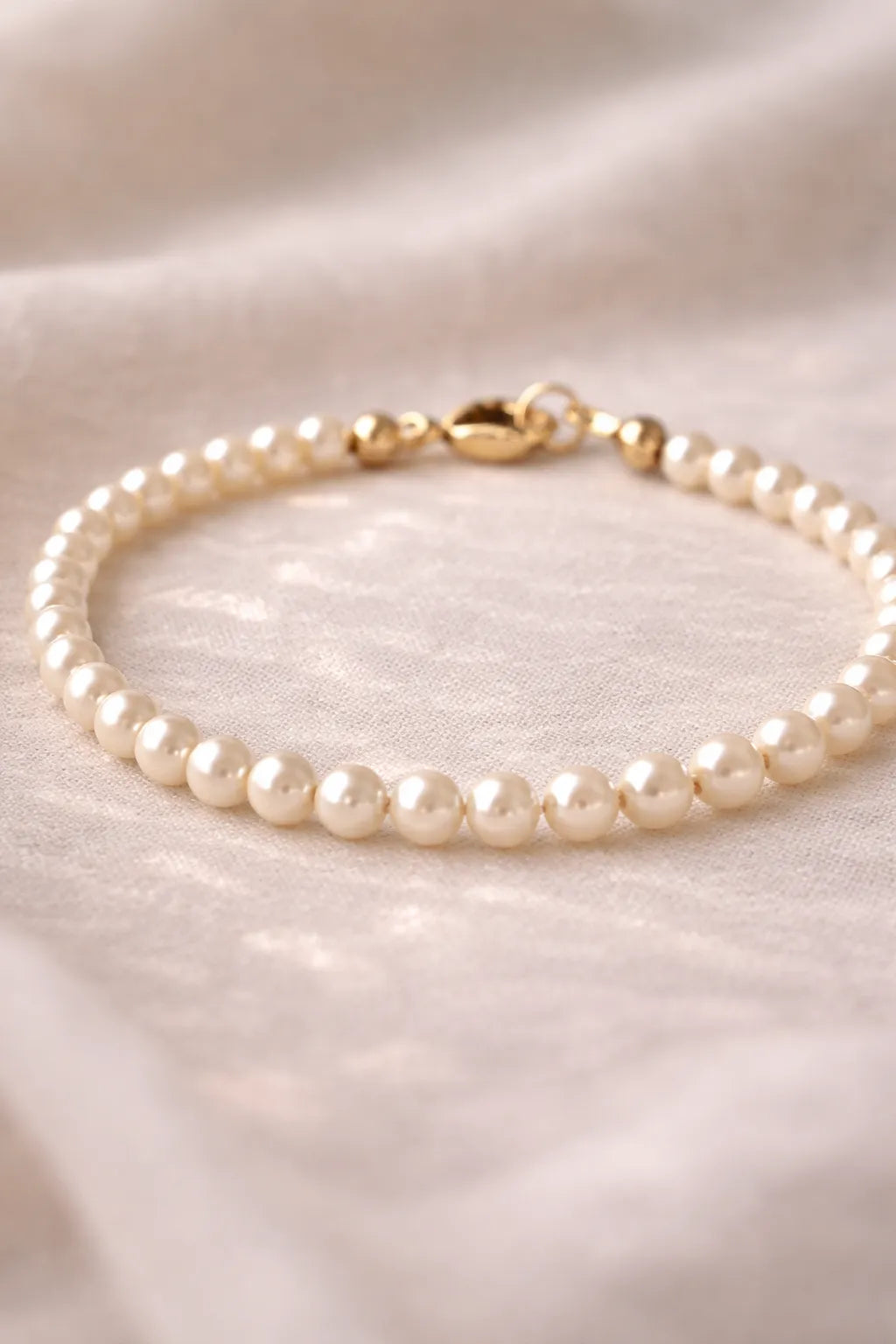 Leilani Cream Pearl Bracelet close-up showing luminous Austrian crystal pearls and a polished 14k gold clasp on a soft neutral fabric background