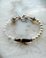 Handcrafted Elodie Pearl & Gemstone Bracelet featuring European crystal pearls, blue chalcedony, Tibetan agate focal bead, and antique silver accents on a luminous stone backdrop