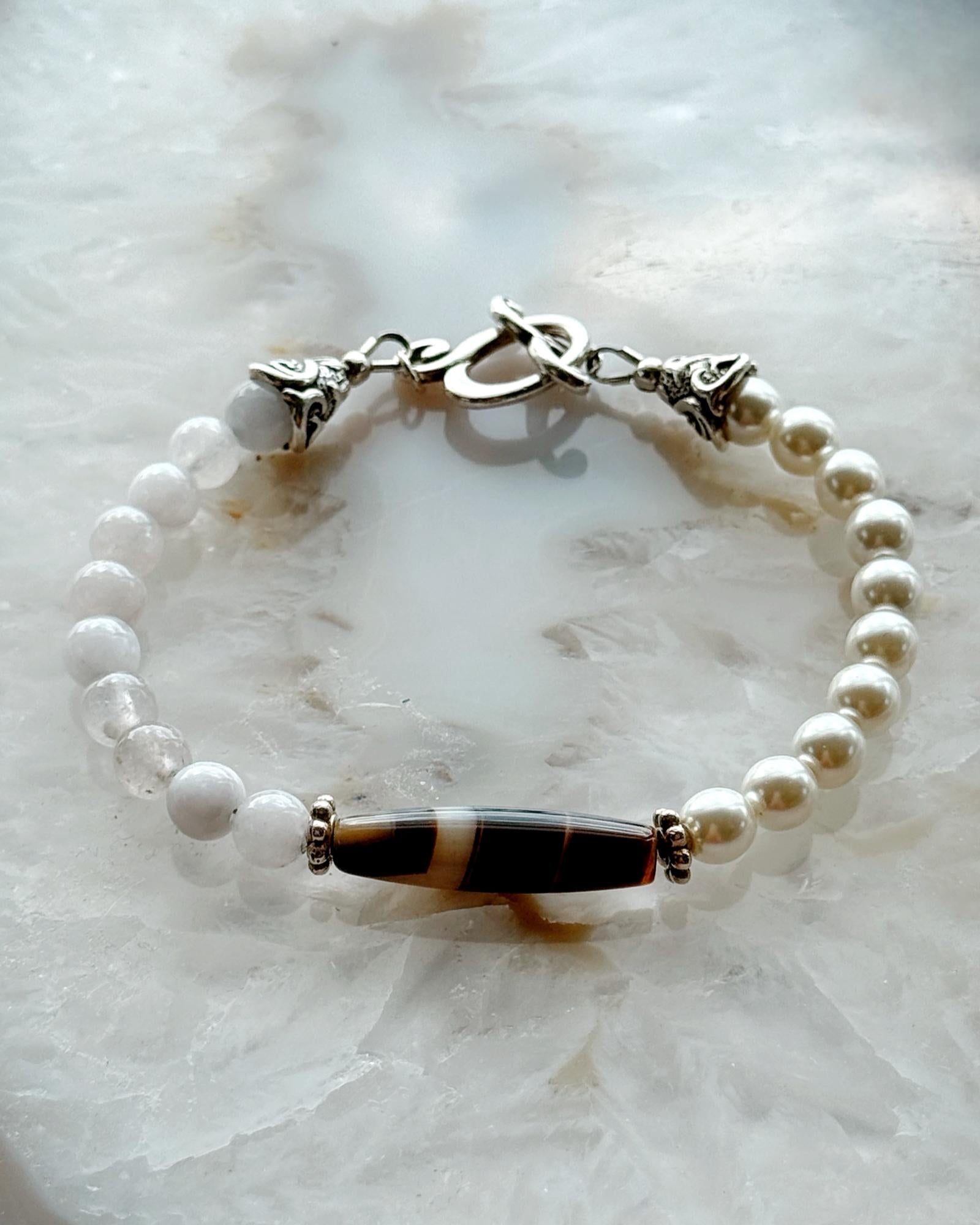 Handcrafted Elodie Pearl & Gemstone Bracelet featuring European crystal pearls, blue chalcedony, Tibetan agate focal bead, and antique silver accents on a luminous stone backdrop