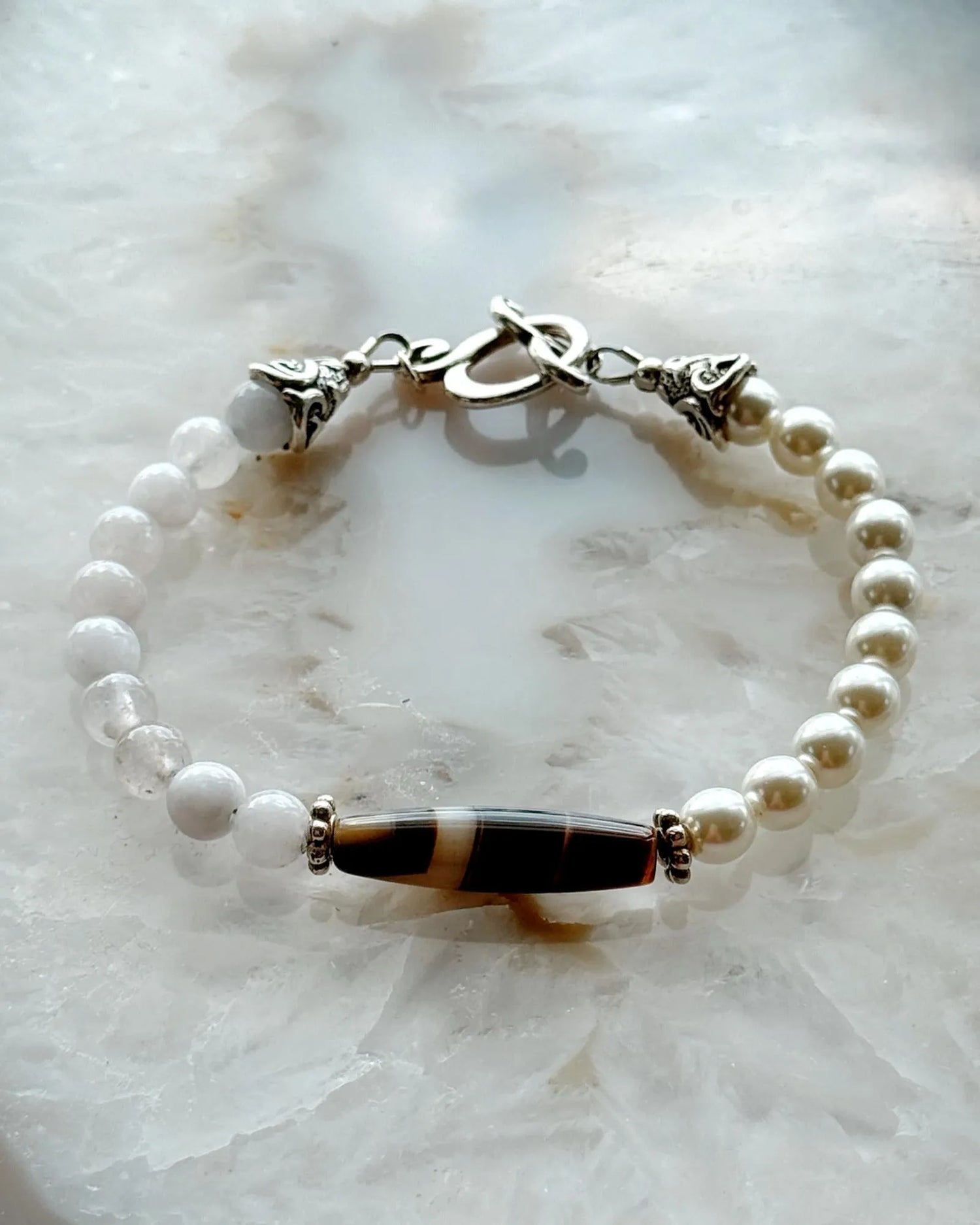 Handcrafted Elodie Pearl & Gemstone Bracelet featuring European crystal pearls, blue chalcedony, Tibetan agate focal bead, and antique silver accents on a luminous stone backdrop