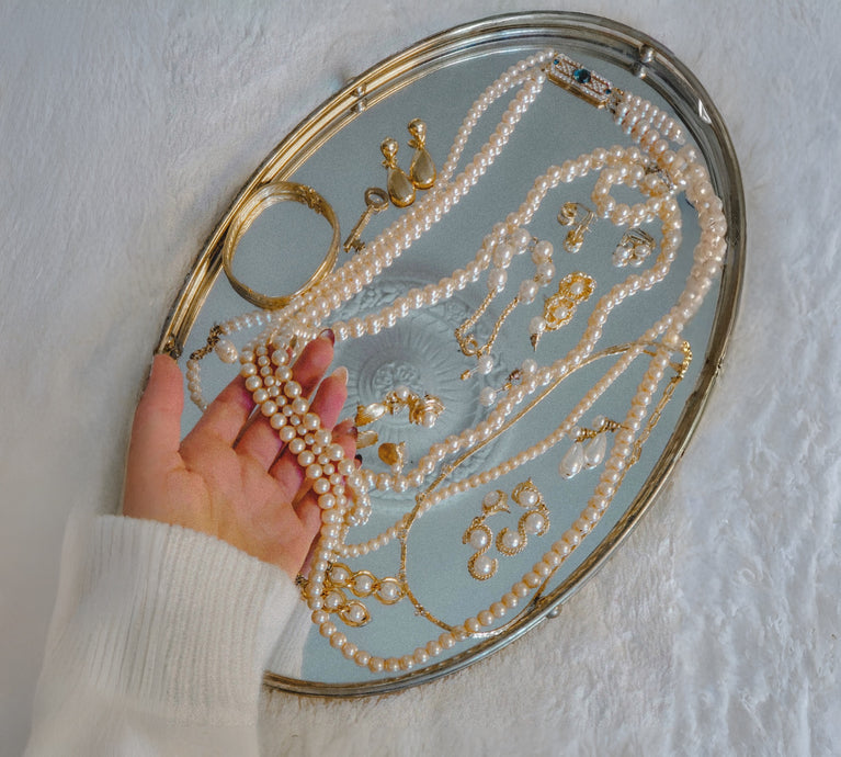 Hand holding pearls over a mirror with jewelry on a white background
