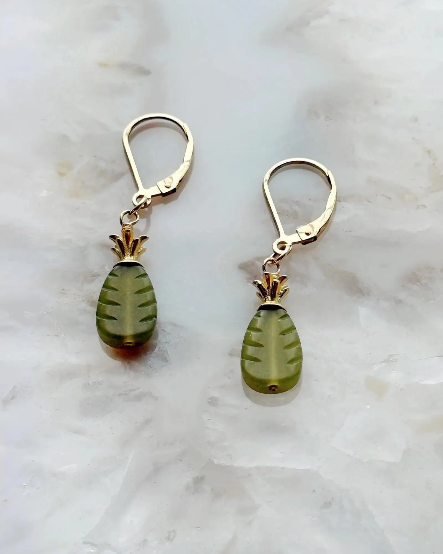 Flat lay of the Layla Carved Jade Earrings featuring richly carved green jade drops and warm 14k gold pineapple accents on a soft stone background.