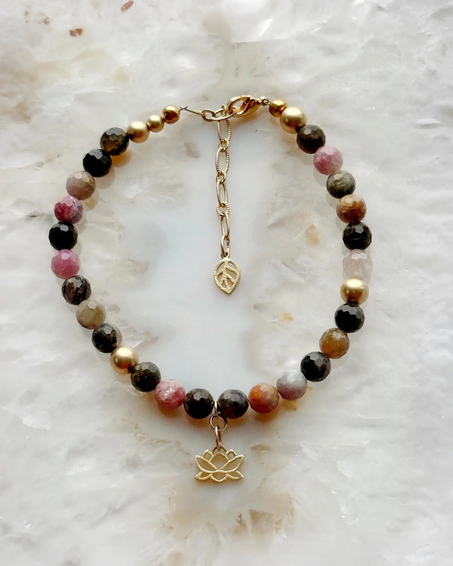 Flat lay of the Layla Gemstone Bracelet featuring rainbow tourmaline gemstones, refined gold accents, and a lotus charm on a soft stone background.