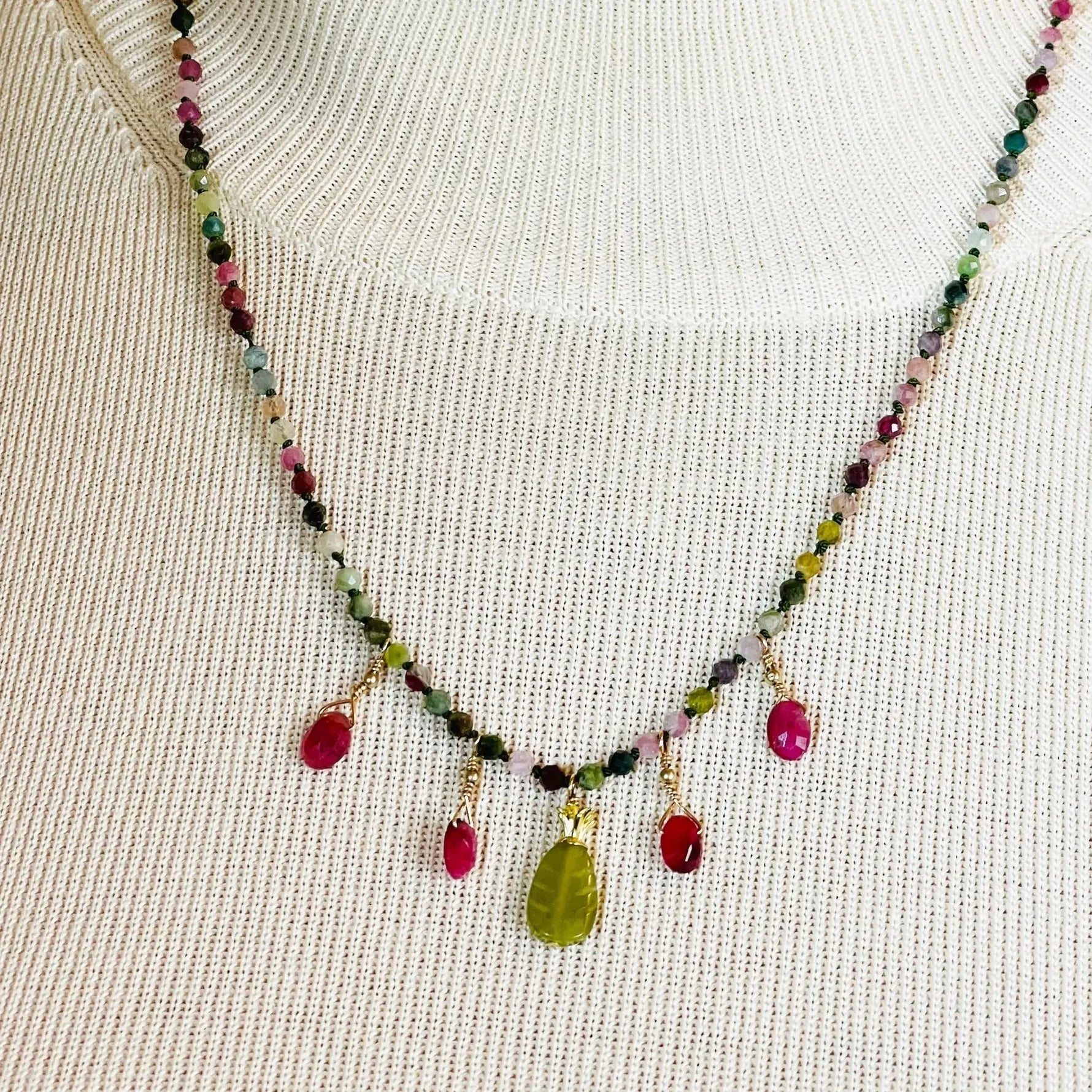 Model wearing the Layla Gemstone Necklace with rainbow tourmaline, ruby drops, and a carved jade leaf pendant styled over a neutral knit top.