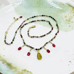 Styled flat lay of the Layla Gemstone Necklace with tourmaline beads, ruby accents, and a carved jade leaf pendant arranged on a ceramic dish.