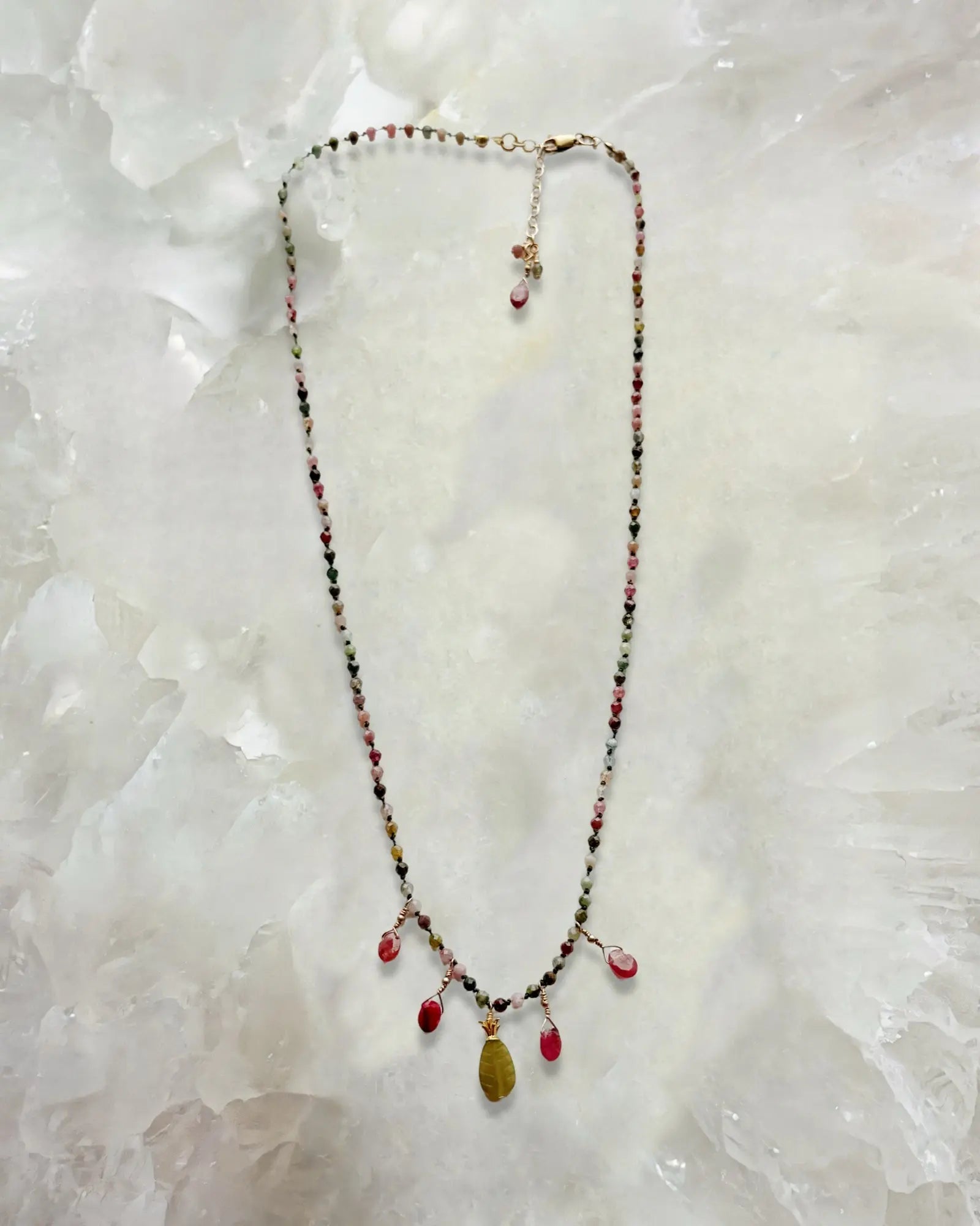 Flat lay of the Layla Gemstone Necklace featuring rainbow tourmaline gemstones, ruby drops, and a carved jade leaf pendant on a soft stone background.