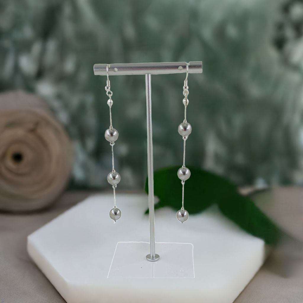 Sterling silver Natasha dripping pearl drop earrings displayed on a minimalist stand, highlighting the long linear design and luminous European crystal pearls.