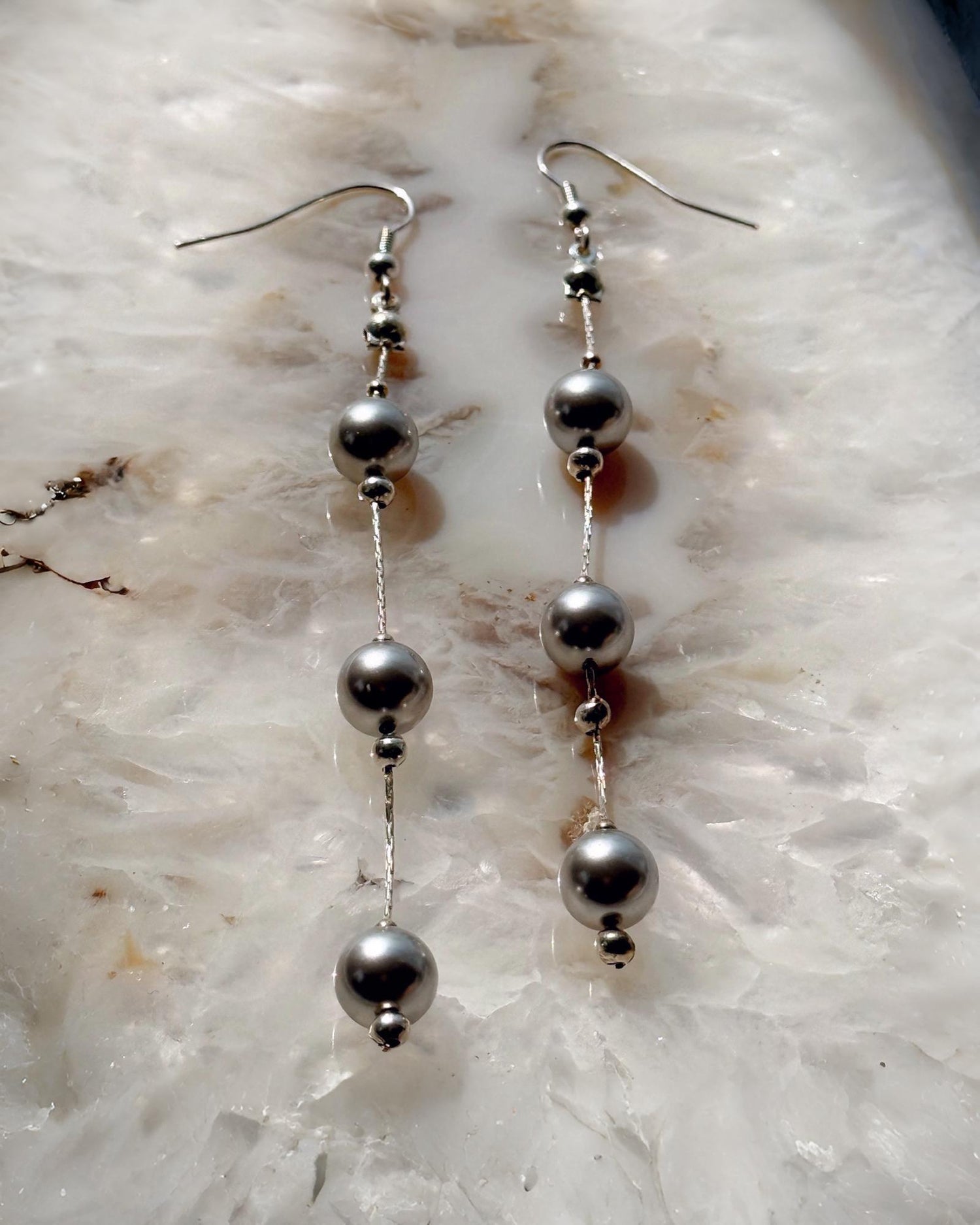 Editorial flat lay of Natasha dripping pearl drop earrings featuring European crystal pearls and sterling silver chain, emphasizing modern pearl styling and refined craftsmanship.