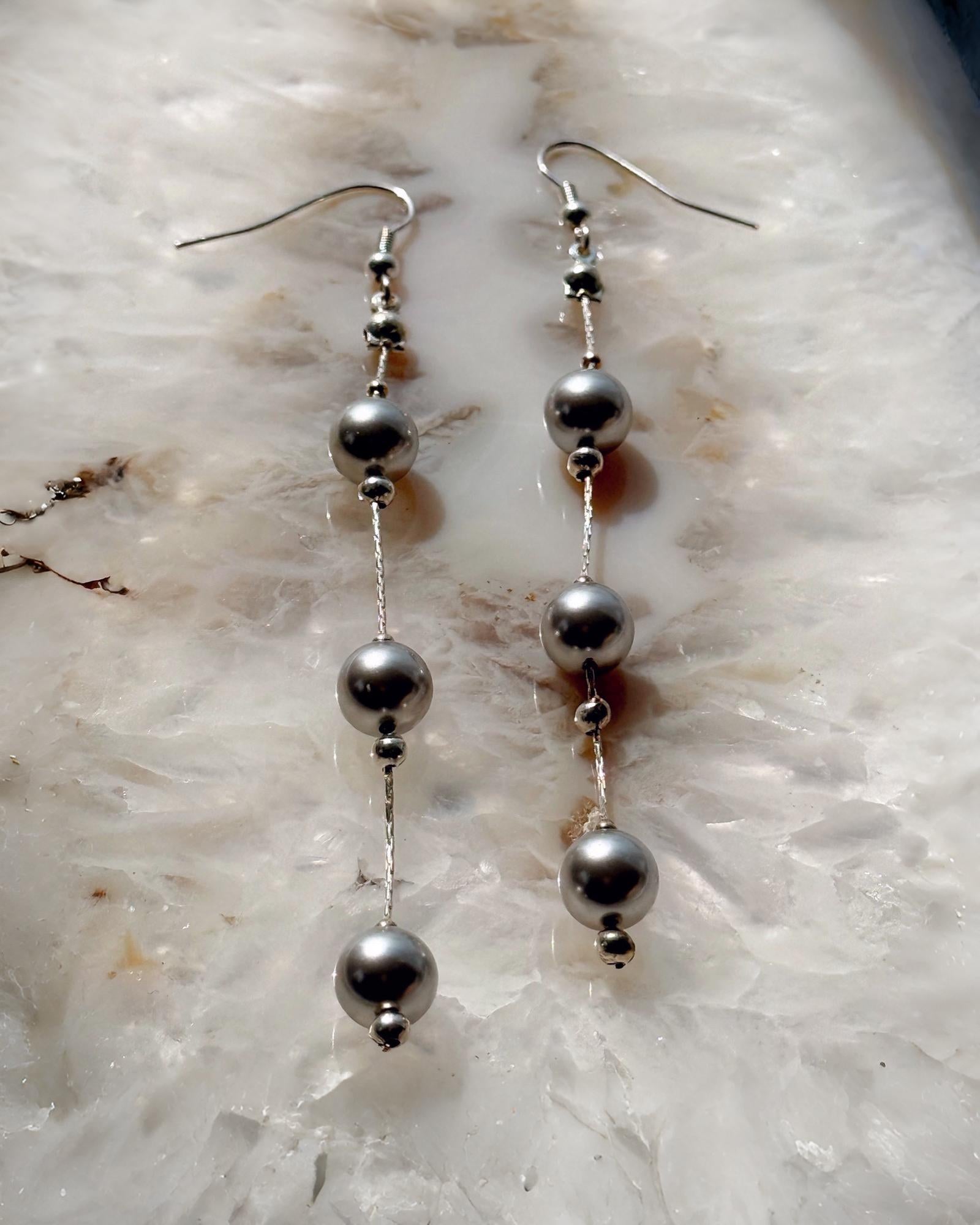 Editorial flat lay of Natasha dripping pearl drop earrings featuring European crystal pearls and sterling silver chain, emphasizing modern pearl styling and refined craftsmanship.