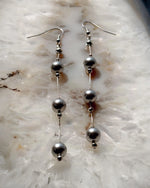 Editorial flat lay of Natasha dripping pearl drop earrings featuring European crystal pearls and sterling silver chain, emphasizing modern pearl styling and refined craftsmanship.