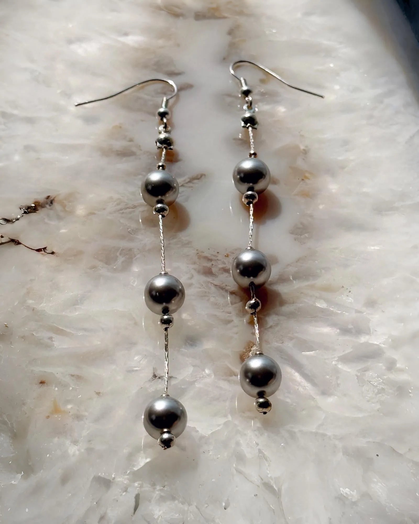 Editorial flat lay of Natasha dripping pearl drop earrings featuring European crystal pearls and sterling silver chain, emphasizing modern pearl styling and refined craftsmanship.