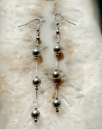 Handcrafted Natasha dripping pearl drop earrings featuring European crystal pearls suspended on sterling silver snake chain, photographed on natural stone for a refined luxury jewelry presentation.