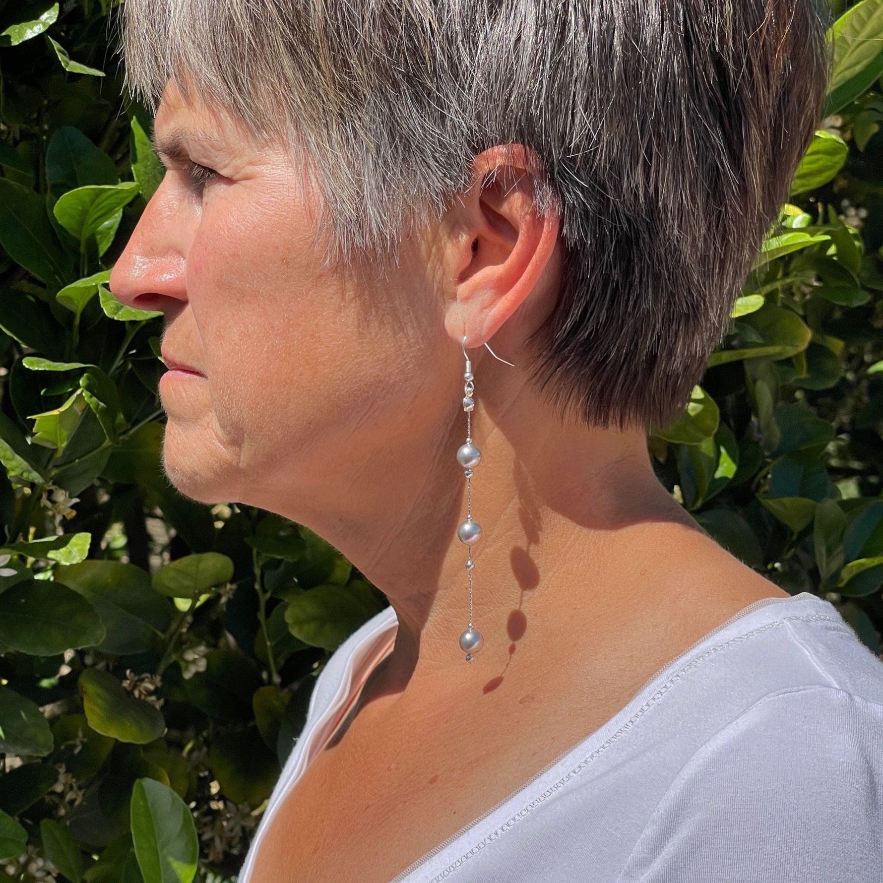 Natasha dripping pearl drop earrings worn in side profile, showcasing elongated sterling silver chain and cascading European crystal pearls with elegant movement and modern sophistication.