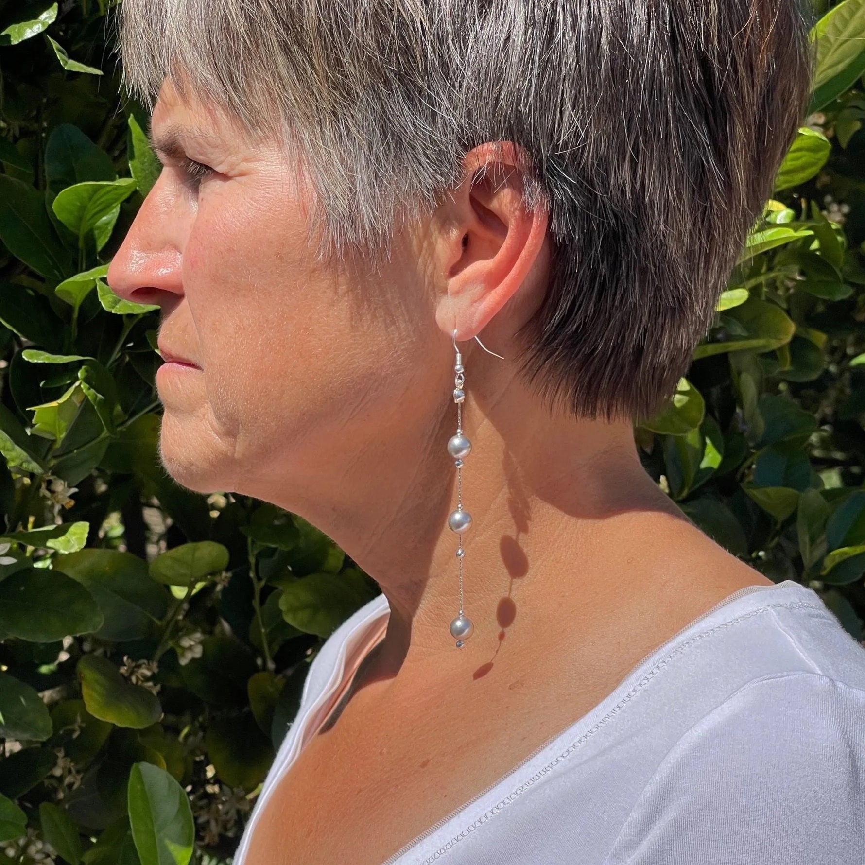 Natasha dripping pearl drop earrings worn in side profile, showcasing elongated sterling silver chain and cascading European crystal pearls with elegant movement and modern sophistication.