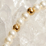Close-up detail of the Noelani Pearl Bracelet showcasing Swarovski® Crystal Pearls, polished gold accent beads, and luxurious craftsmanship on white quartz crystals.