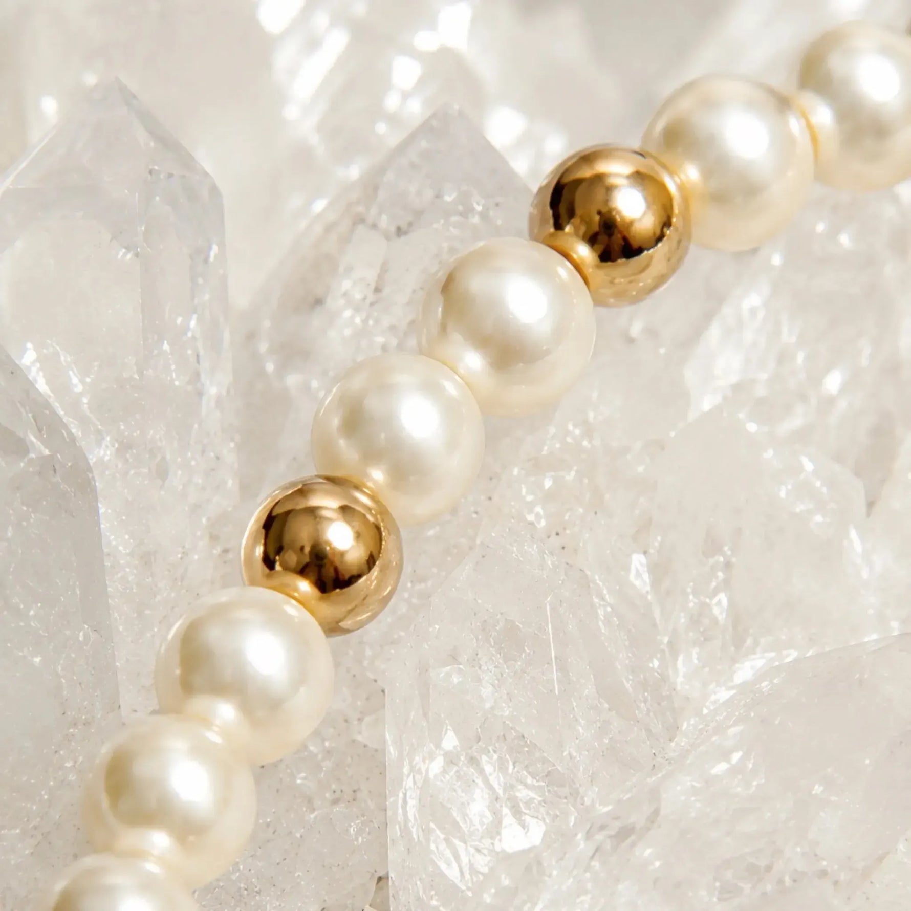 Close-up detail of the Noelani Pearl Bracelet showcasing Swarovski® Crystal Pearls, polished gold accent beads, and luxurious craftsmanship on white quartz crystals.