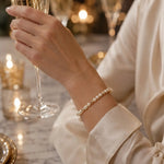 The Noelani Pearl Bracelet featuring luminous Swarovski® Crystal Pearls and gold accents worn during an elegant evening celebration with prosecco.