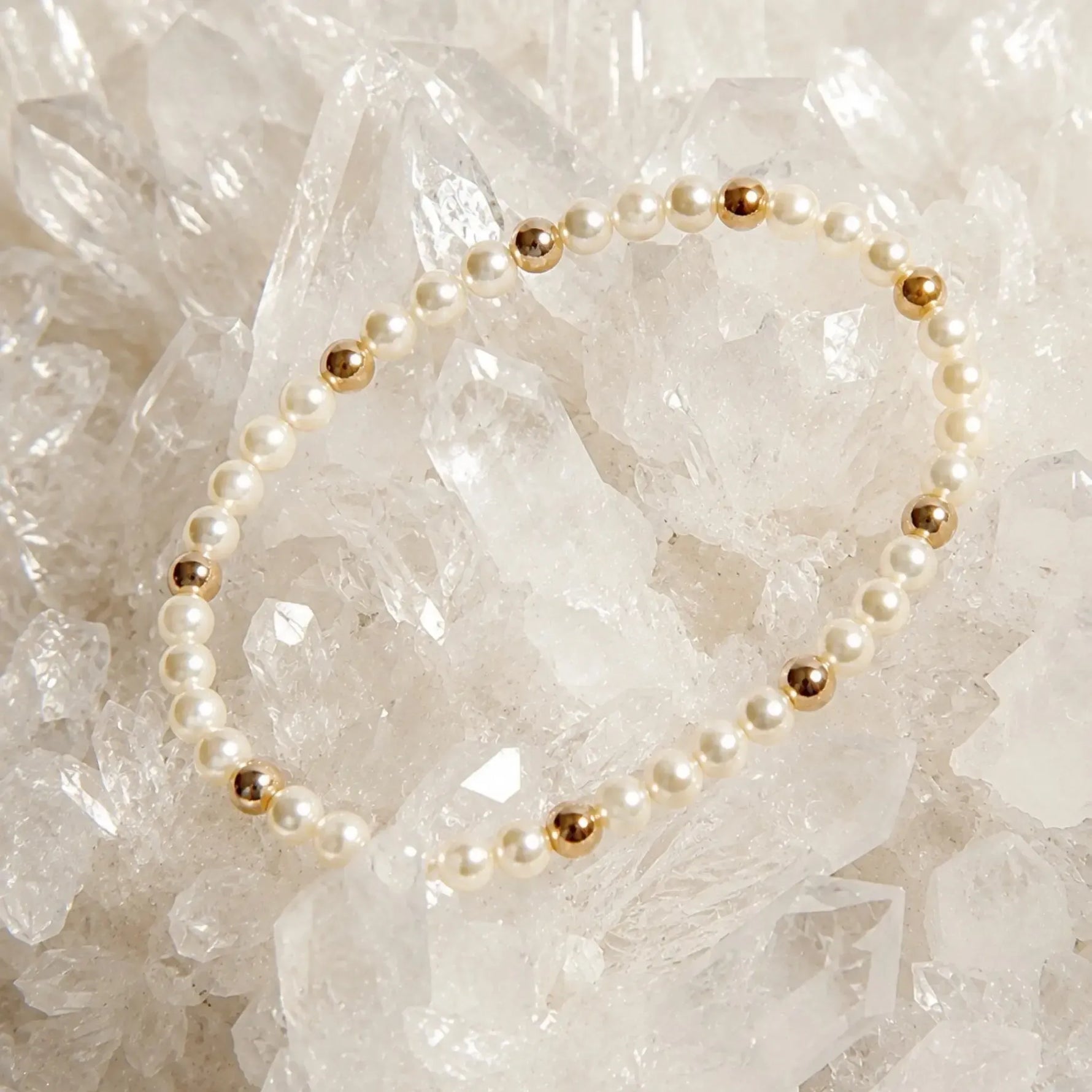 The Noelani Pearl Bracelet arranged atop luminous white quartz crystals, highlighting Swarovski® Crystal Pearls and gold accents.