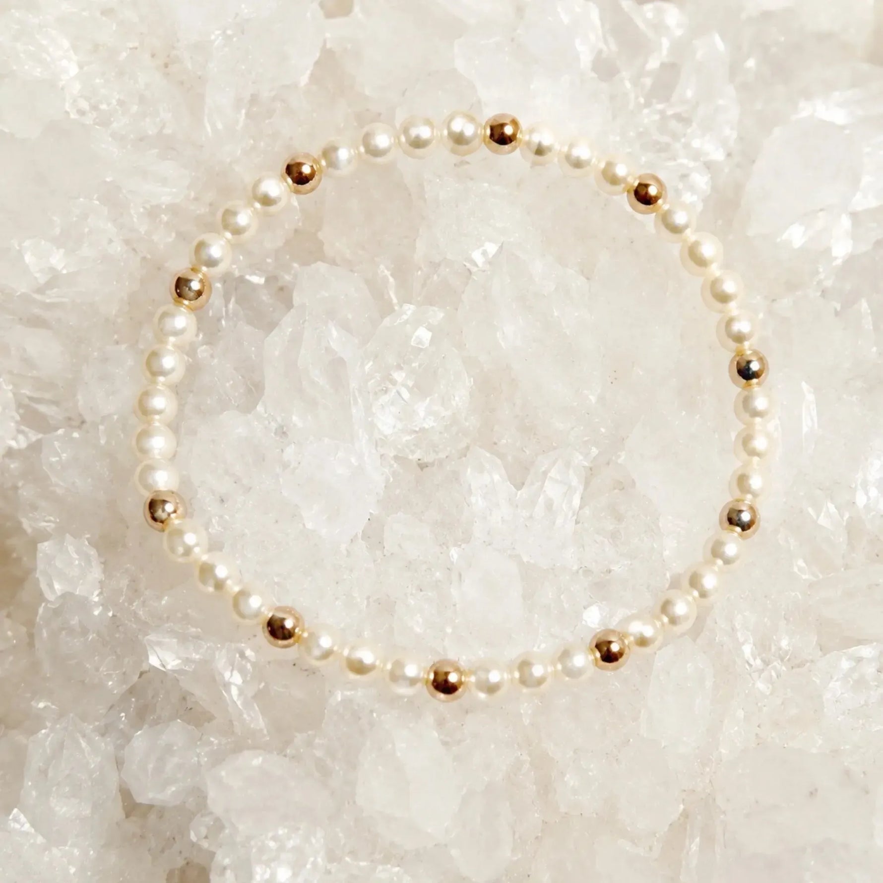 The Noelani Pearl Bracelet featuring Swarovski® Crystal Pearls and gold accents displayed in a circular design on white quartz crystals.