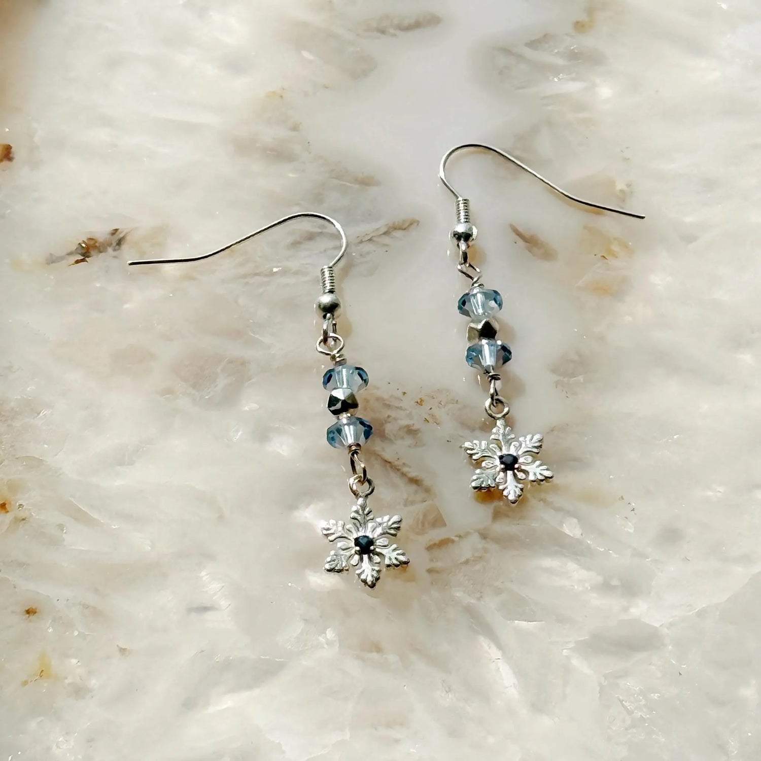 Detail view of the Sapphire Snowflake Earrings showcasing light blue European crystals, a sterling silver snowflake design, and a subtle lab-grown sapphire accent, highlighting refined winter elegance.