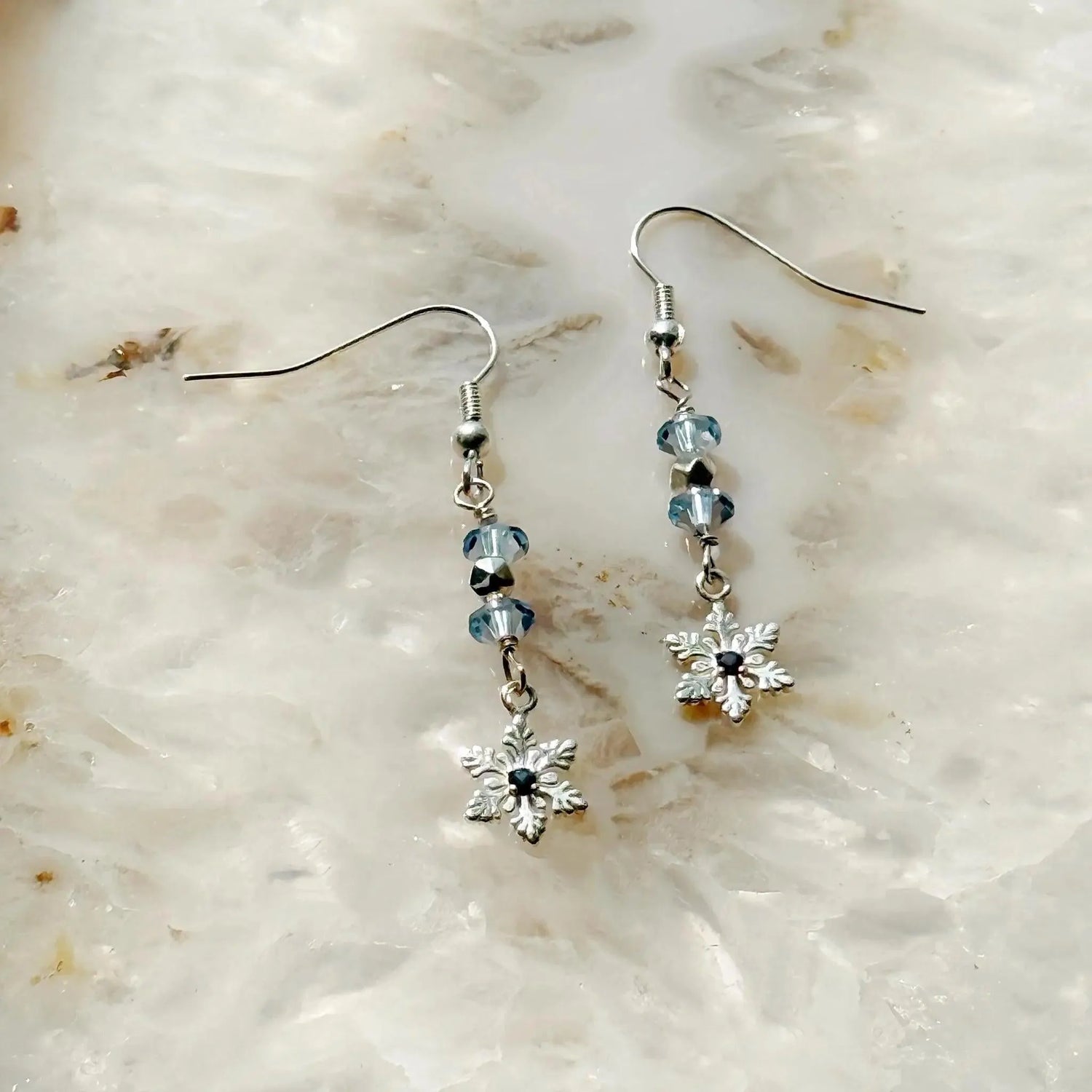 Detail view of the Sapphire Snowflake Earrings showcasing light blue European crystals, a sterling silver snowflake design, and a subtle lab-grown sapphire accent, highlighting refined winter elegance.