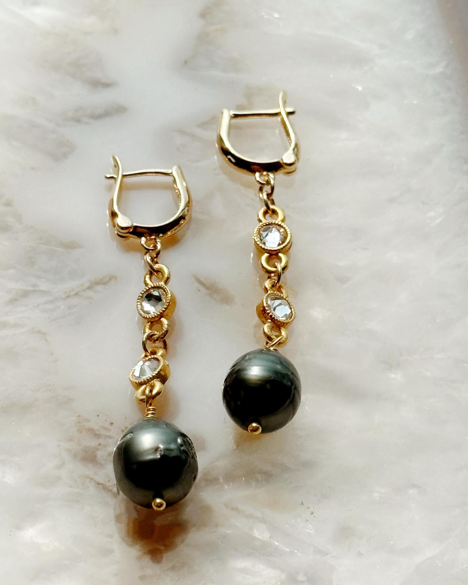 Close-up of Tahitian South Sea black pearl earrings with gold bezel-set crystals on a quartz background by Carabella by Cheryl.