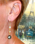 Model wearing Tahitian South Sea black pearl earrings with gold accents and crystal connectors by Carabella by Cheryl.