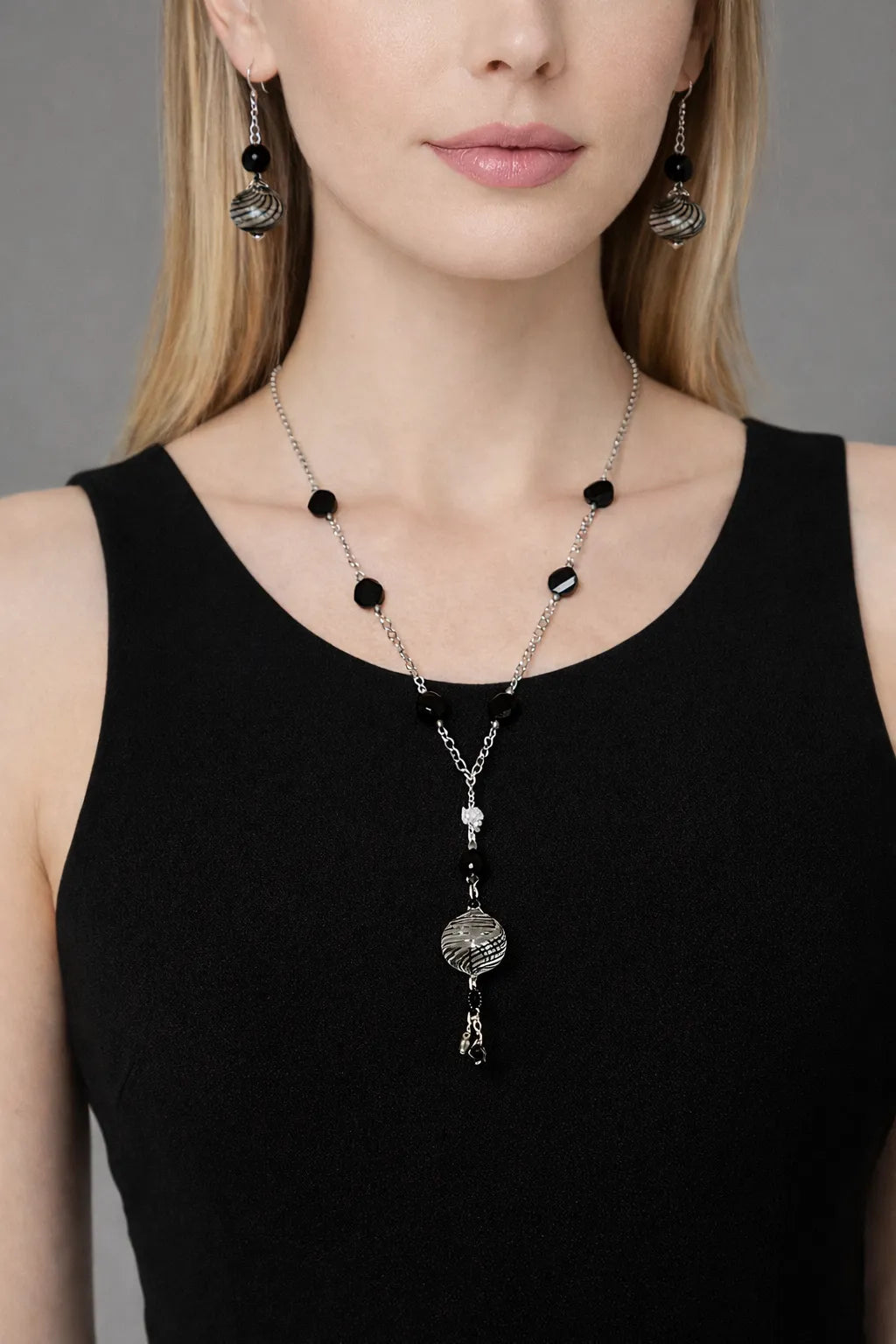 Venezia black Murano glass necklace and matching earrings with silver chain and faceted black beads, worn with a sleeveless black dress in a refined studio setting.