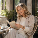 Woman reading a book on a café terrace while wearing the Ainsley Miyuki Tila Bracelet, reflecting quiet confidence, comfort, and refined everyday elegance.