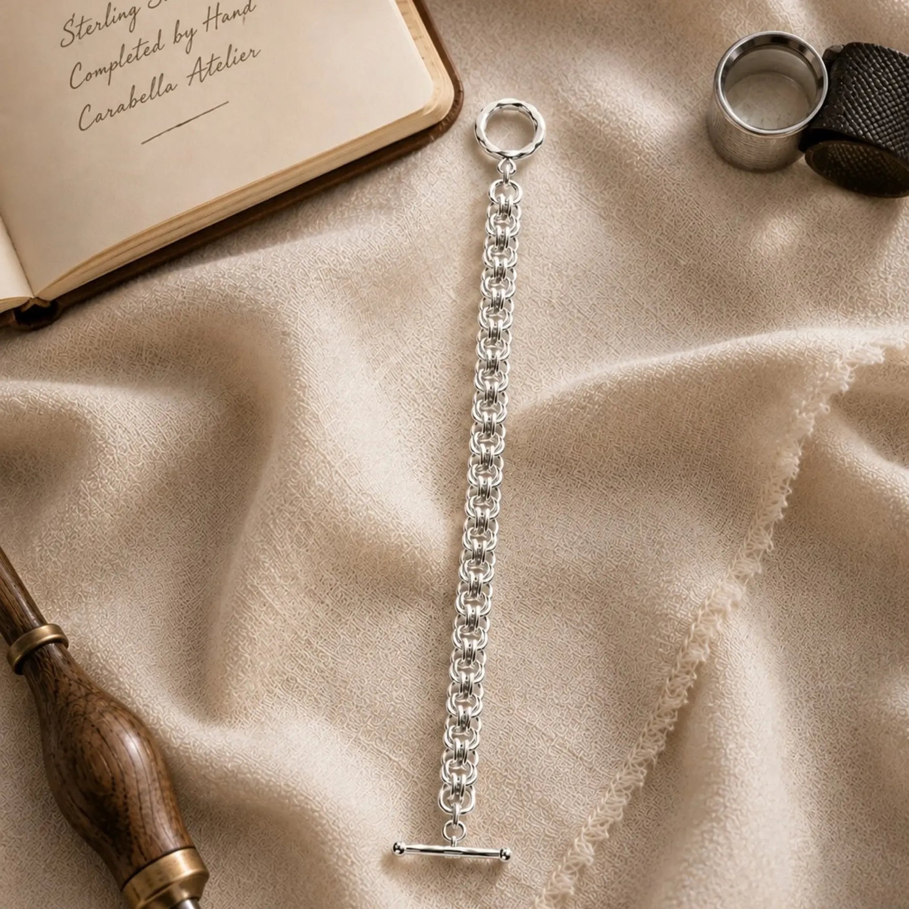 Avalon sterling silver Celtic helm bracelet displayed in the Carabella atelier beside a design journal and jewellery-making tools.