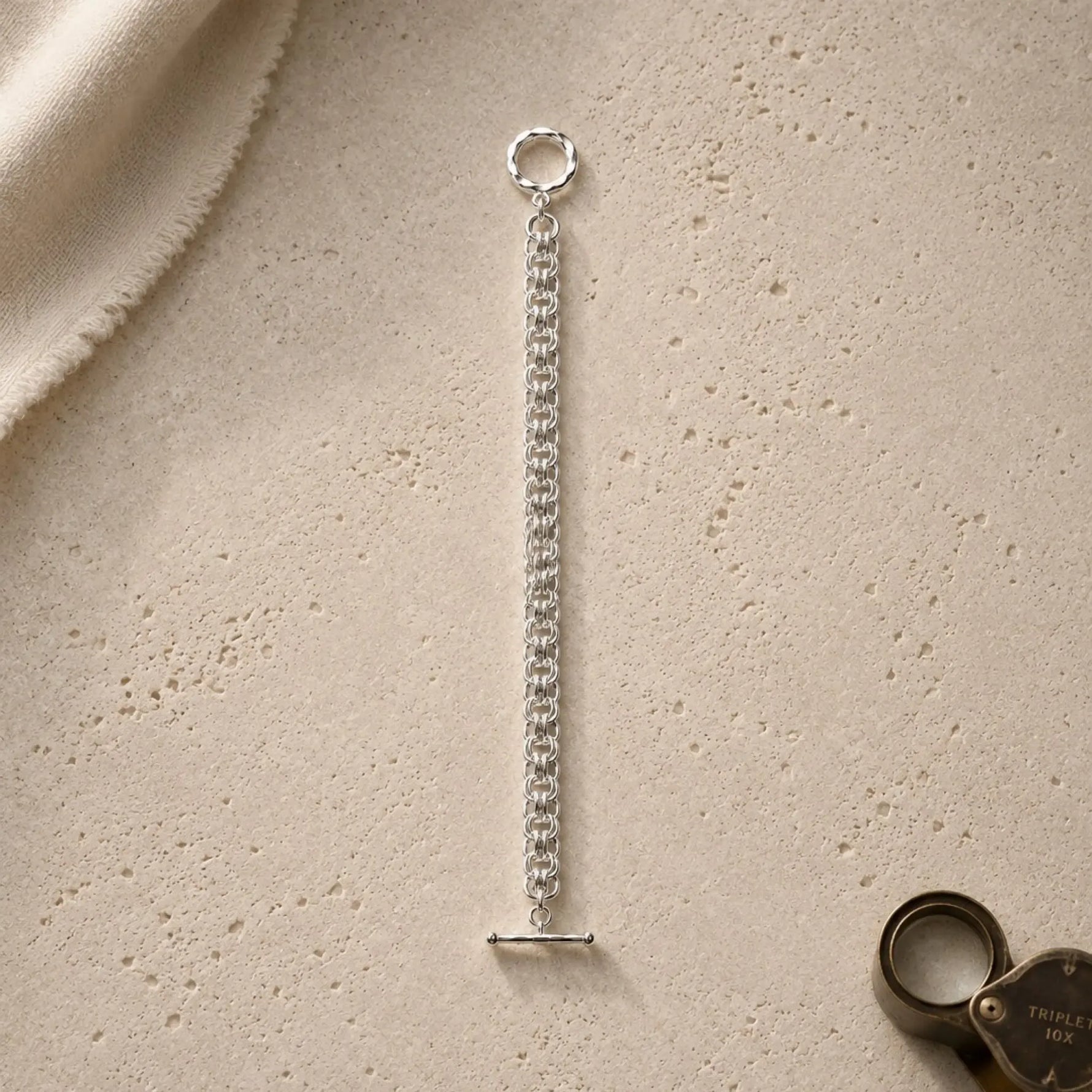 Avalon sterling silver Celtic helm bracelet presented on warm limestone with an antique jeweller’s loupe and ivory conservation cloth.