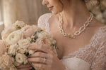 Bride holding an ivory and blush bouquet wearing a freshwater pearl necklace with gold accents, romantic bridal jewelry styled with lace wedding gown.