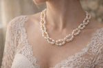 Bride wearing a freshwater pearl necklace with gold accents, close-up neckline view with lace wedding dress in soft natural bridal light.