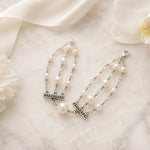 Editorial flat lay of the Calla pearl bracelet styled with ivory ribbon and white florals on a refined stone surface.
