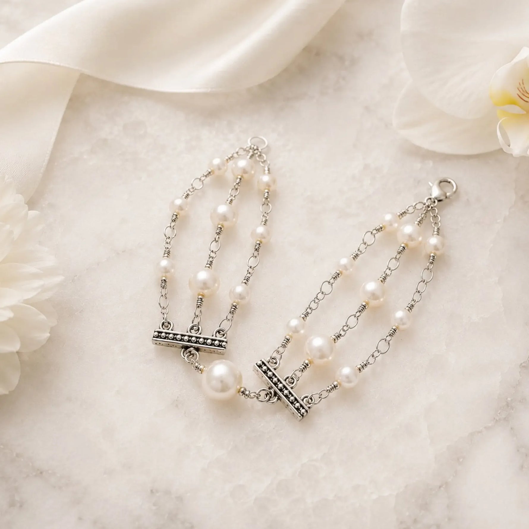 Editorial flat lay of the Calla pearl bracelet styled with ivory ribbon and white florals on a refined stone surface.