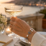 Calla Swarovski® Crystal Pearl bracelet worn during an elegant evening toast overlooking a waterfront terrace at sunset.