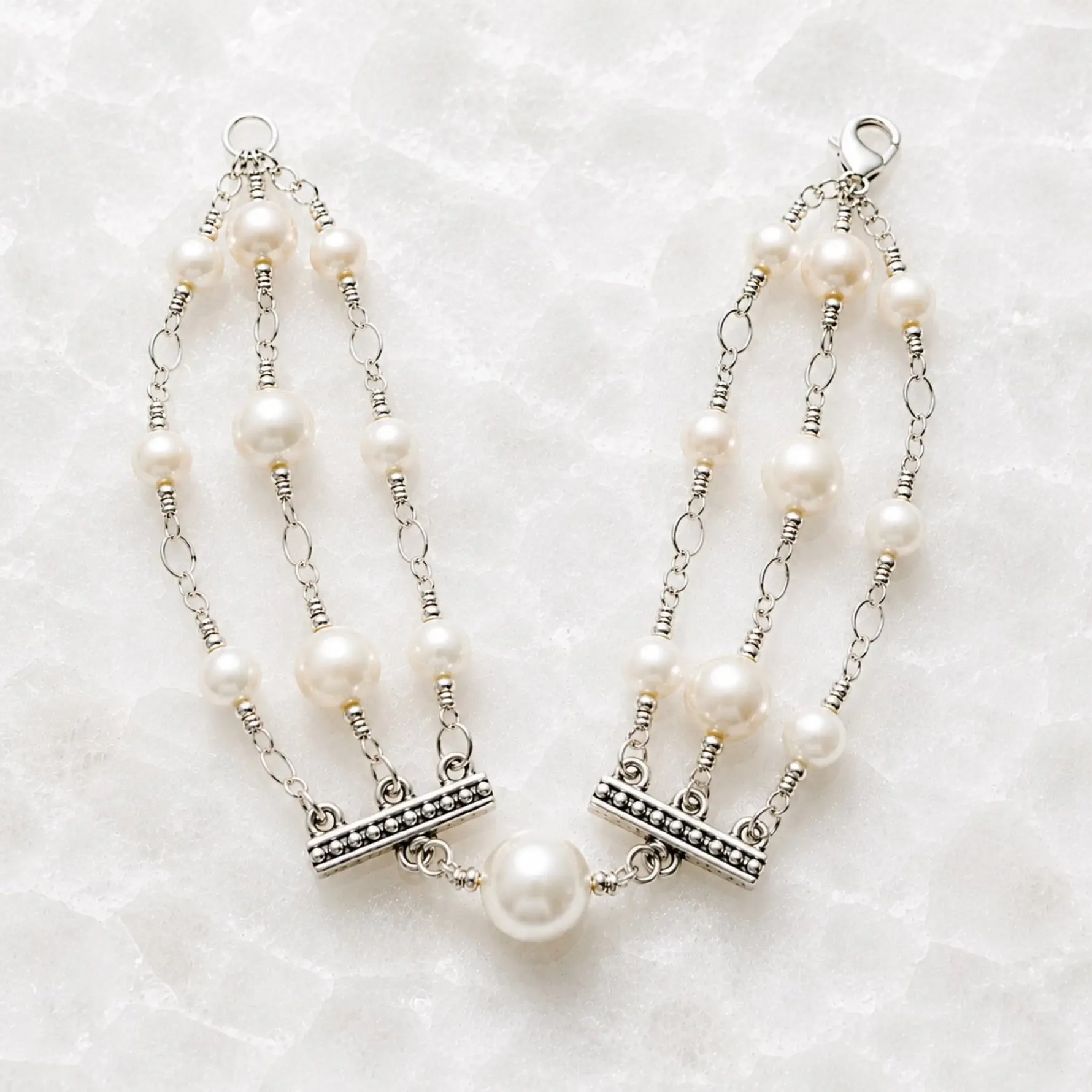 Calla handcrafted triple strand Swarovski® Crystal Pearl bracelet with sterling silver accents on a white quartz background.