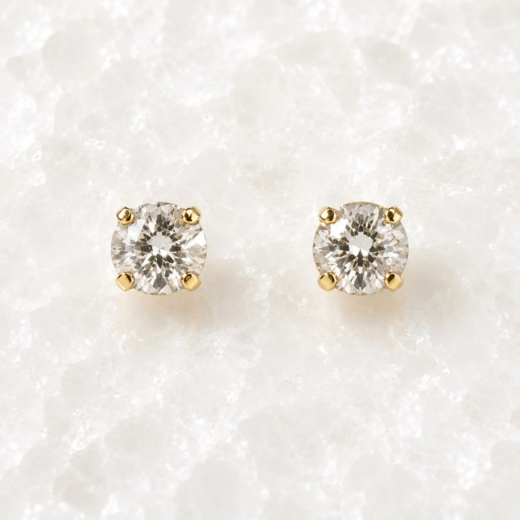 Capri Gold Crystal Stud Earrings featuring brilliant round European crystals in a classic four-prong champagne gold setting displayed on the Carabella white quartz slab.