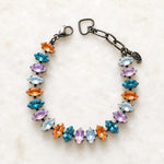 Capri Multi-Color Crystal Tennis Bracelet featuring marquise-cut crystals in aqua, lavender, white and orange set in a gunmetal finish, photographed on Carabella's signature white quartz background.