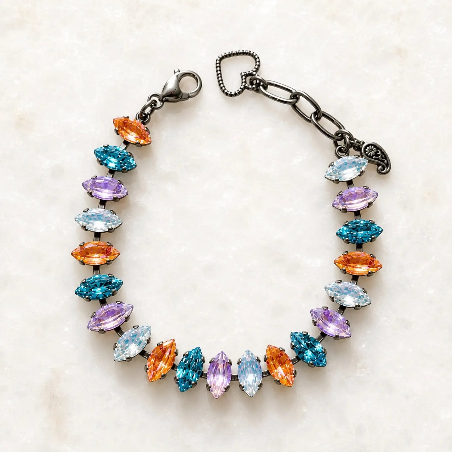 Capri Multi-Color Crystal Tennis Bracelet featuring marquise-cut crystals in aqua, lavender, white and orange set in a gunmetal finish, photographed on Carabella's signature white quartz background.