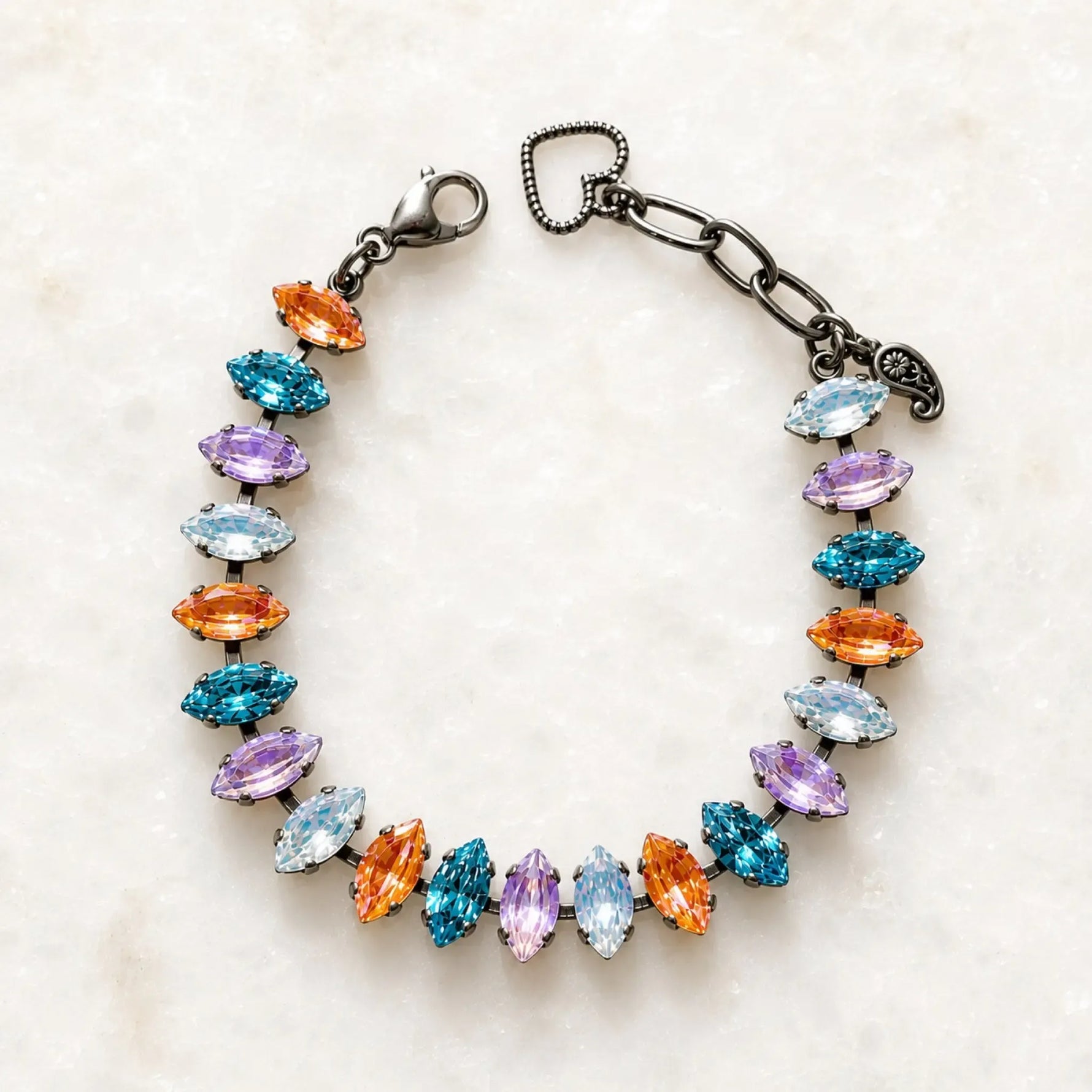 Capri Multi-Color Crystal Tennis Bracelet featuring marquise-cut crystals in aqua, lavender, white and orange set in a gunmetal finish, photographed on Carabella's signature white quartz background.
