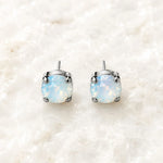 Capri Opal Crystal Stud Earrings featuring luminous round opal crystals in polished silver settings on Carabella's signature white quartz background.