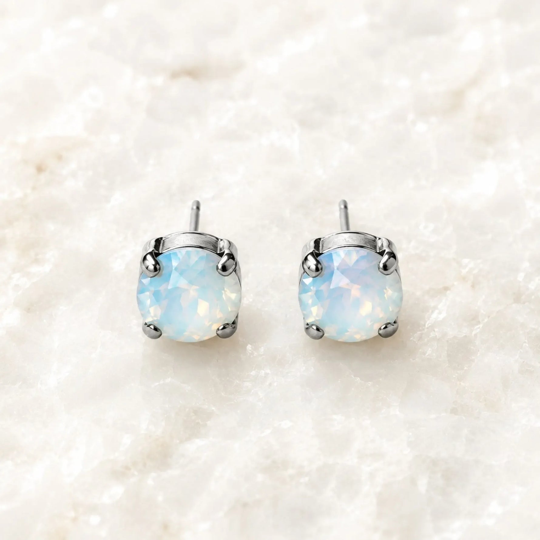 Capri Opal Crystal Stud Earrings featuring luminous round opal crystals in polished silver settings on Carabella's signature white quartz background.